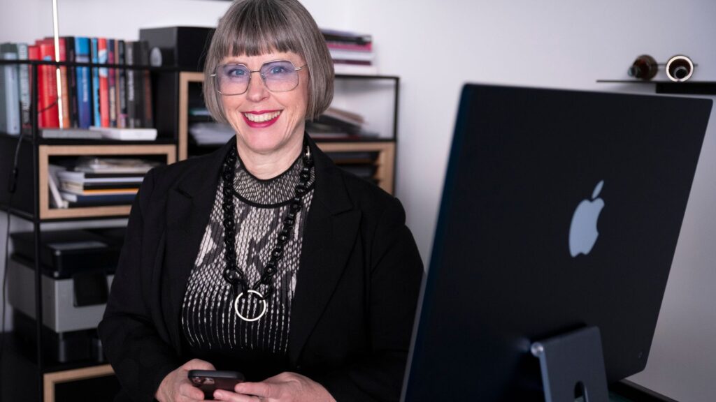 Karin Stehr an ihrem Schreibtisch mit iMac und Handy im BĂĽro